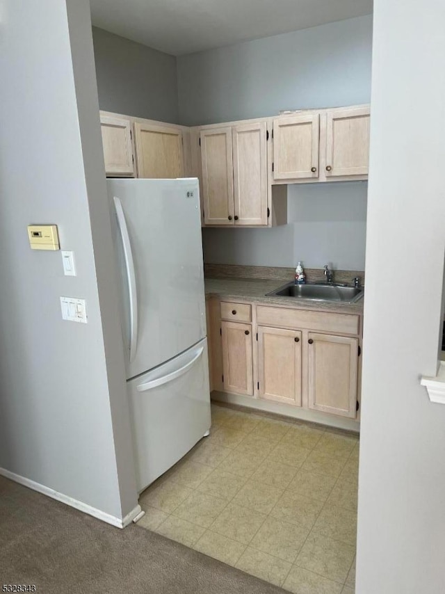 kitchen with a sink, baseboards, freestanding refrigerator, and light brown cabinets