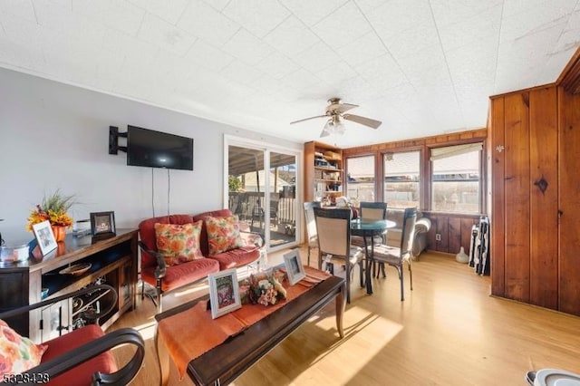 living room featuring ceiling fan, wood walls, and light wood-type flooring