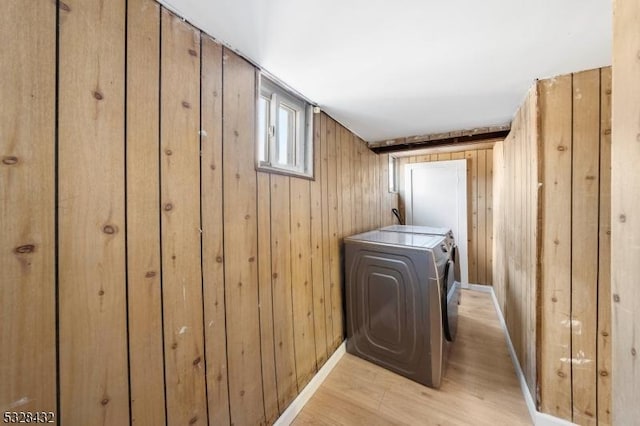 washroom featuring washer and dryer, light wood-type flooring, and wooden walls