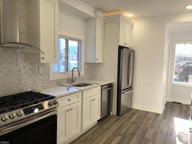 kitchen with dark wood-type flooring, white cabinets, wall chimney range hood, light stone counters, and stainless steel appliances