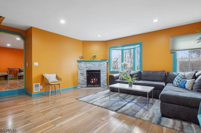 living room with hardwood / wood-style floors, a healthy amount of sunlight, and a stone fireplace