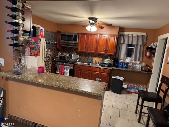 kitchen with kitchen peninsula, a kitchen breakfast bar, tasteful backsplash, stainless steel appliances, and stone counters