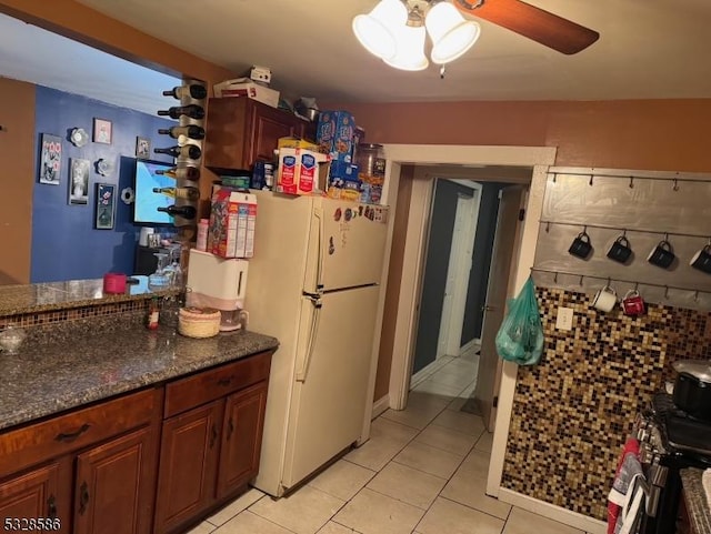 kitchen featuring ceiling fan, white fridge, dark stone countertops, and light tile patterned floors