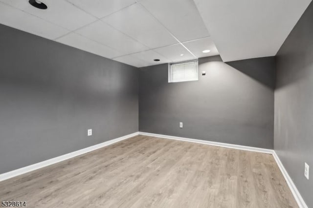 basement featuring a paneled ceiling and light hardwood / wood-style floors