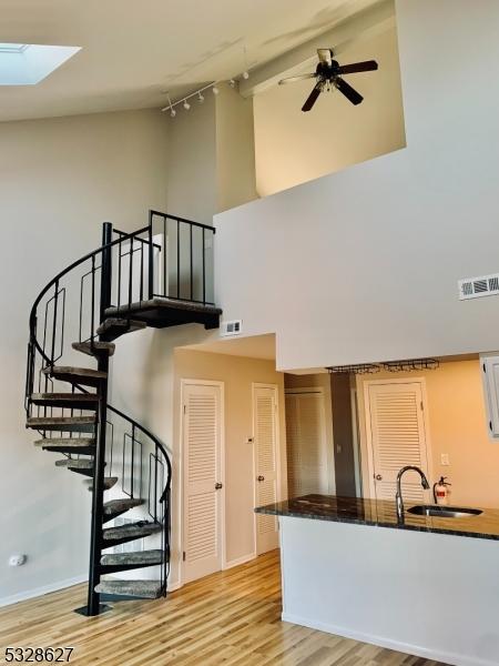 kitchen featuring a towering ceiling, light wood-type flooring, a skylight, and sink