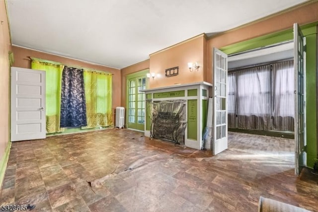 unfurnished living room featuring a wealth of natural light, radiator heating unit, and french doors