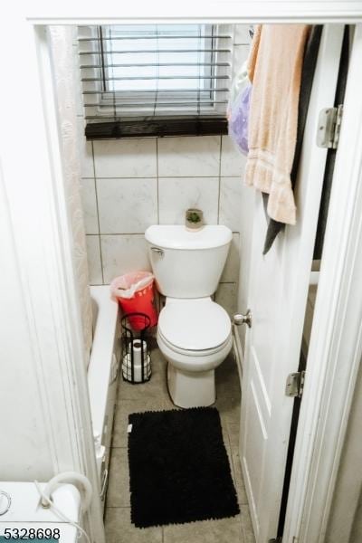 bathroom with toilet, a bathtub, and tile walls