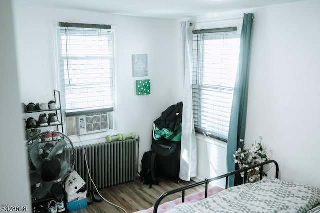 bedroom featuring cooling unit, radiator, multiple windows, and wood finished floors