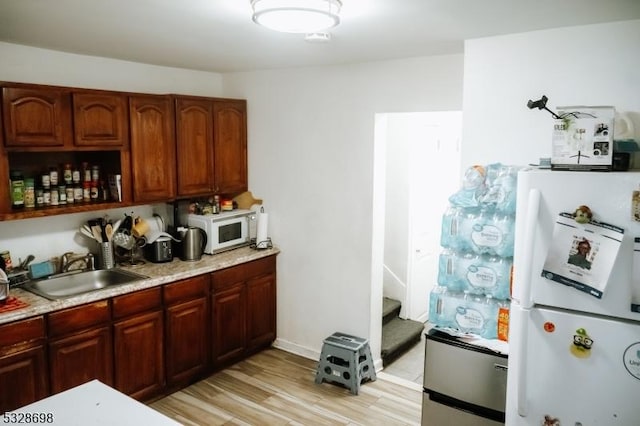 kitchen featuring light wood-type flooring, white appliances, light countertops, and a sink