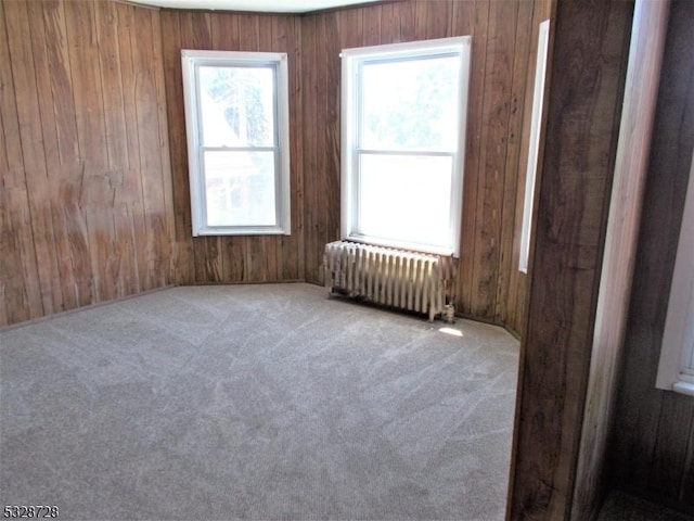 carpeted spare room featuring wooden walls and radiator heating unit