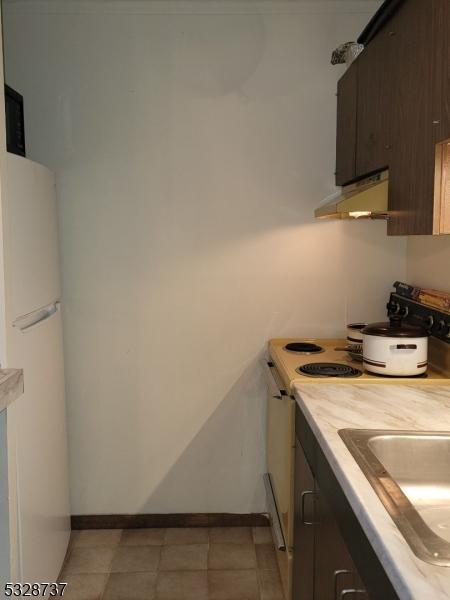 kitchen with light tile patterned flooring, dark brown cabinetry, white appliances, and sink