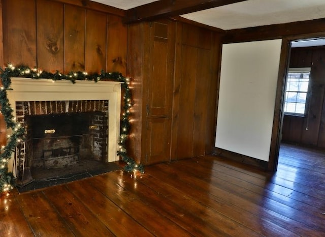 unfurnished living room featuring wooden walls, dark wood-type flooring, and a brick fireplace