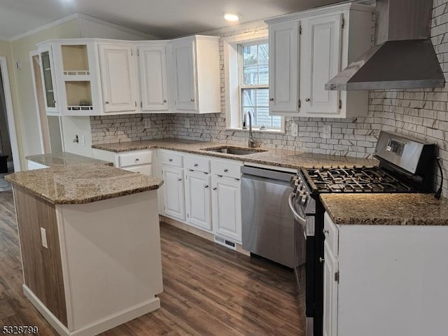 kitchen with light stone countertops, stainless steel appliances, a kitchen island, wall chimney range hood, and white cabinetry