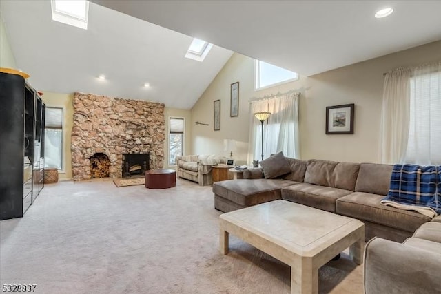 carpeted living room featuring a healthy amount of sunlight, lofted ceiling with skylight, and a stone fireplace