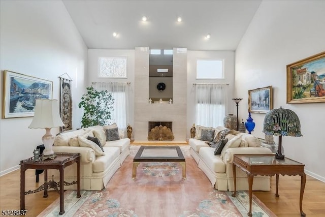 living room with light wood-type flooring, a large fireplace, plenty of natural light, and a high ceiling