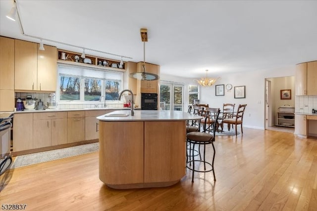 kitchen featuring an island with sink, decorative backsplash, decorative light fixtures, light brown cabinetry, and sink