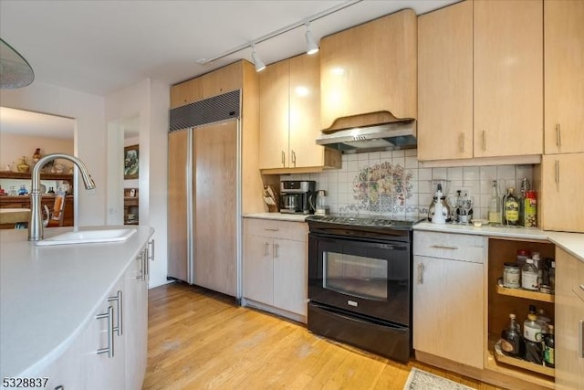 kitchen featuring paneled refrigerator, light brown cabinetry, sink, black electric range oven, and range hood