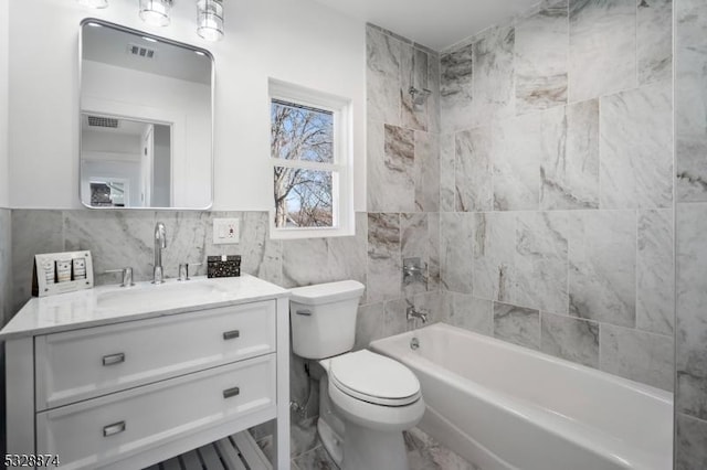 full bathroom featuring vanity, tiled shower / bath combo, toilet, and tile walls