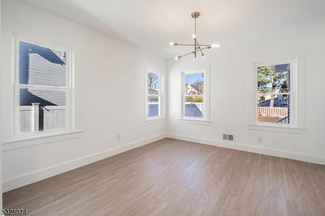 unfurnished room featuring a chandelier, hardwood / wood-style floors, and a healthy amount of sunlight
