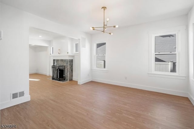 unfurnished living room with hardwood / wood-style floors, a notable chandelier, and a fireplace