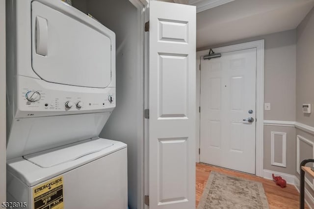 laundry room with crown molding, stacked washing maching and dryer, and light wood-type flooring