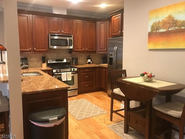 kitchen featuring sink, light stone counters, light wood-type flooring, stainless steel appliances, and decorative backsplash