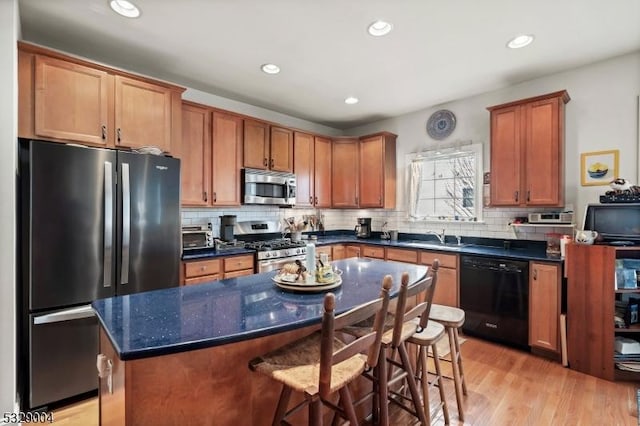 kitchen featuring a kitchen breakfast bar, dark stone counters, light hardwood / wood-style floors, a kitchen island, and appliances with stainless steel finishes