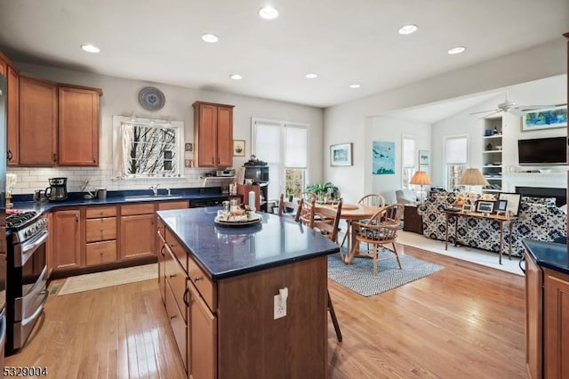 kitchen featuring decorative backsplash, stainless steel gas range oven, ceiling fan, sink, and light hardwood / wood-style floors