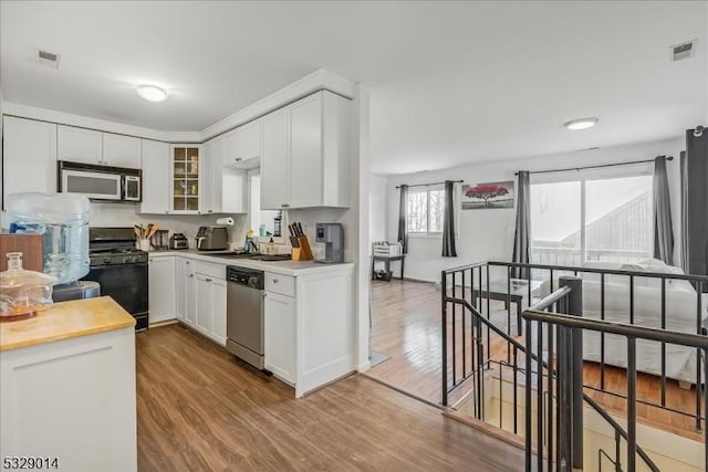 kitchen with black gas range, white cabinetry, sink, light hardwood / wood-style flooring, and stainless steel dishwasher