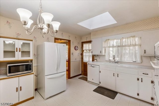 kitchen with a skylight, sink, decorative light fixtures, white appliances, and white cabinets