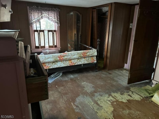 bedroom with radiator, dark wood-type flooring, and wooden walls