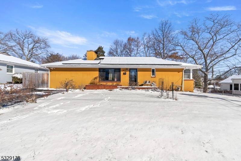 snow covered rear of property featuring solar panels