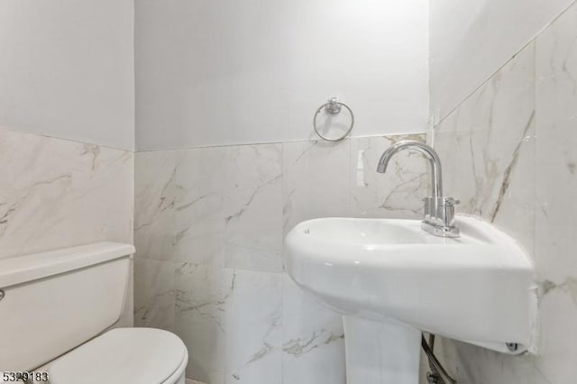 bathroom with toilet, sink, and tile walls