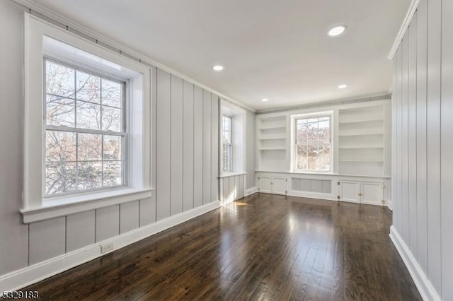 unfurnished room featuring built in shelves, plenty of natural light, crown molding, and dark wood-type flooring