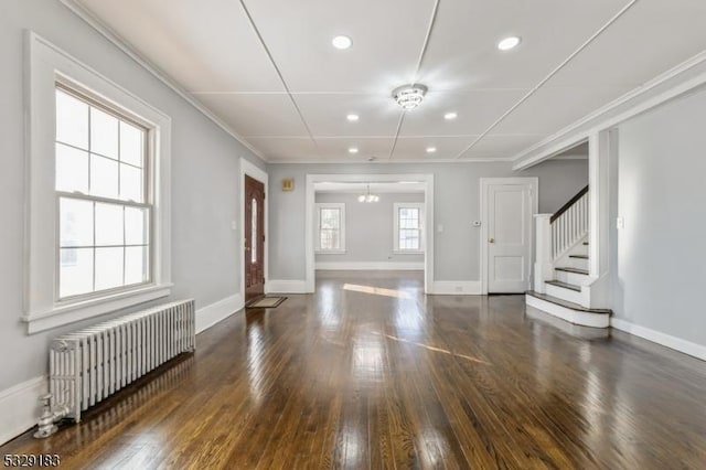 interior space with dark hardwood / wood-style flooring, radiator heating unit, ornamental molding, and an inviting chandelier