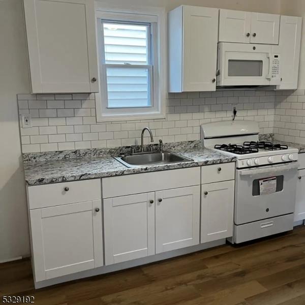 kitchen with light stone counters, sink, white cabinets, and white appliances