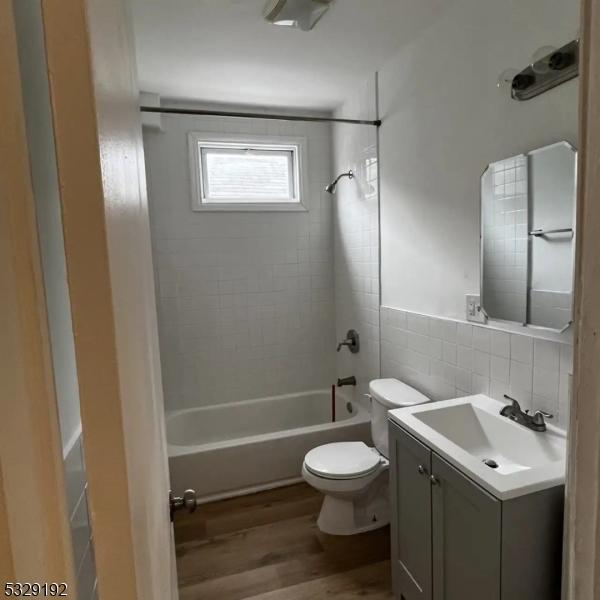 full bathroom with hardwood / wood-style floors, vanity, tiled shower / bath combo, toilet, and tile walls