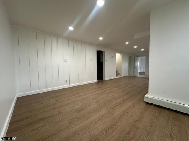 unfurnished room featuring a baseboard heating unit, recessed lighting, wood finished floors, and baseboards