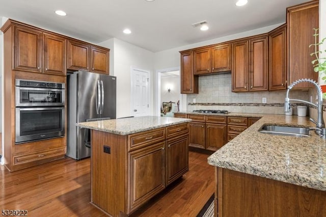 kitchen with appliances with stainless steel finishes, light stone counters, a kitchen island, and sink