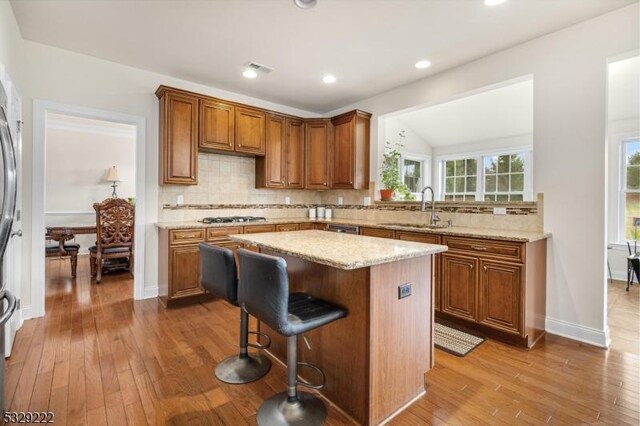 kitchen with light stone countertops, sink, stainless steel gas stovetop, decorative backsplash, and a kitchen island