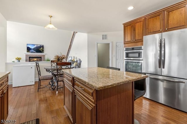 kitchen featuring light stone countertops, a brick fireplace, pendant lighting, a kitchen island, and appliances with stainless steel finishes