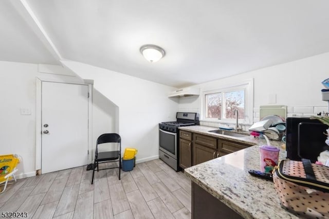 kitchen featuring light stone countertops, dark brown cabinets, gas stove, and sink