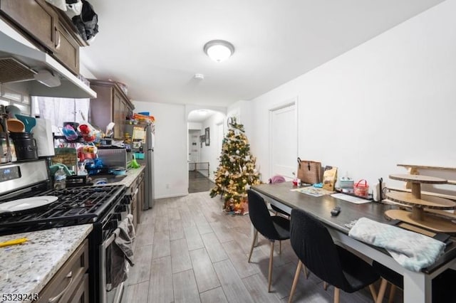 kitchen featuring stainless steel gas range oven, light stone countertops, and dark brown cabinets