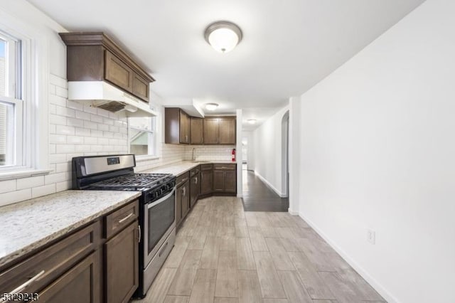 kitchen with decorative backsplash, light wood-type flooring, light stone countertops, gas stove, and dark brown cabinetry