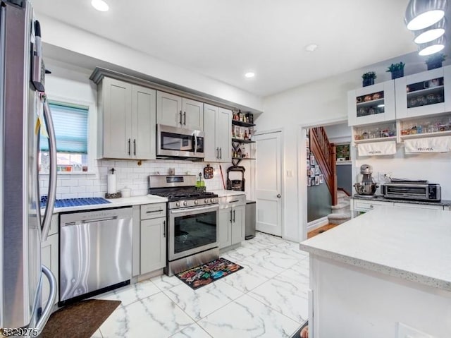 kitchen with appliances with stainless steel finishes, backsplash, gray cabinets, and hanging light fixtures