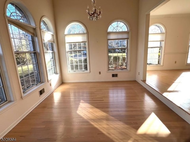 empty room with plenty of natural light, light hardwood / wood-style floors, and an inviting chandelier