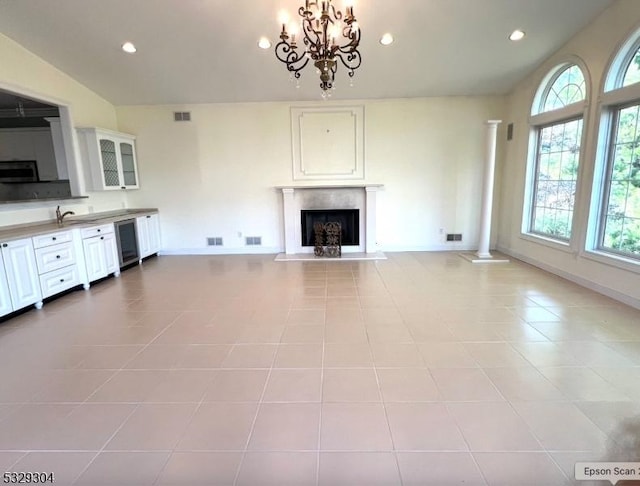 unfurnished living room with decorative columns, an inviting chandelier, and light tile patterned flooring