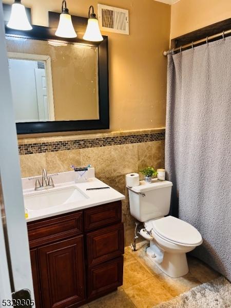 bathroom featuring tile patterned floors, vanity, tile walls, and toilet