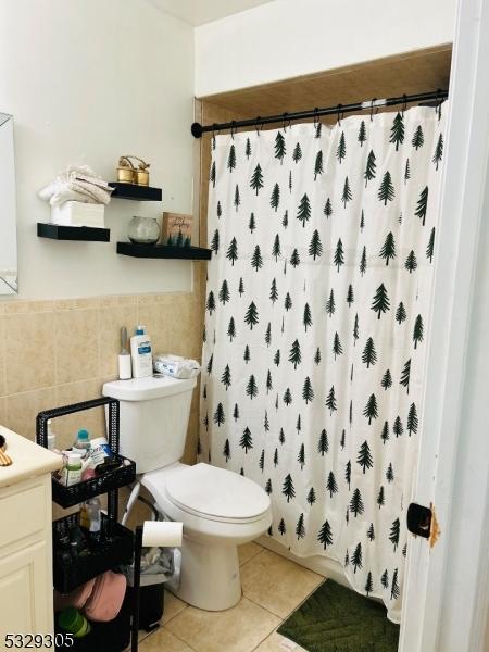 bathroom featuring walk in shower, vanity, tile walls, tile patterned flooring, and toilet