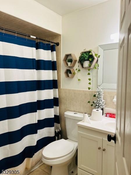 bathroom with walk in shower, vanity, tile walls, tile patterned flooring, and toilet